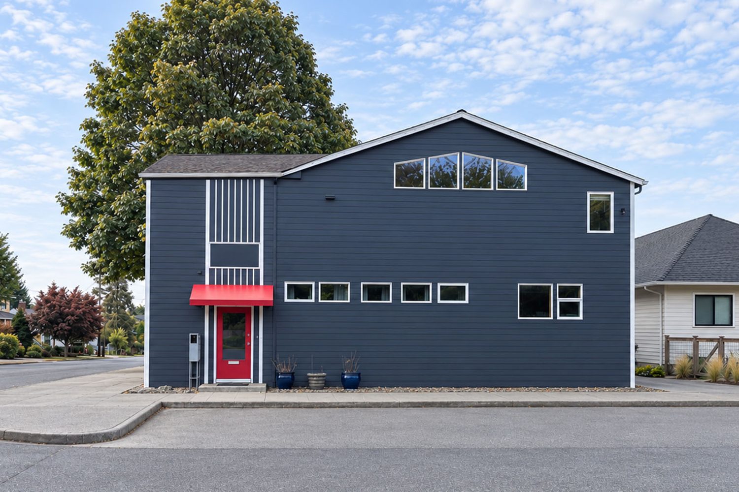 Studio Space Ballard at the corner of 28th and 70th: a two-story charcoal building with white window trim, a red door under a red awning, and a white slatted entry bay.